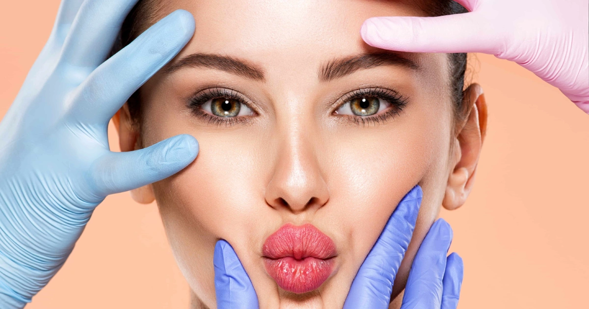 Close-up of a woman’s face being gently touched by pink and blue gloved hands, hinting at a cosmetic or medical procedure, Plastic Surgery in Whitefish, MT.